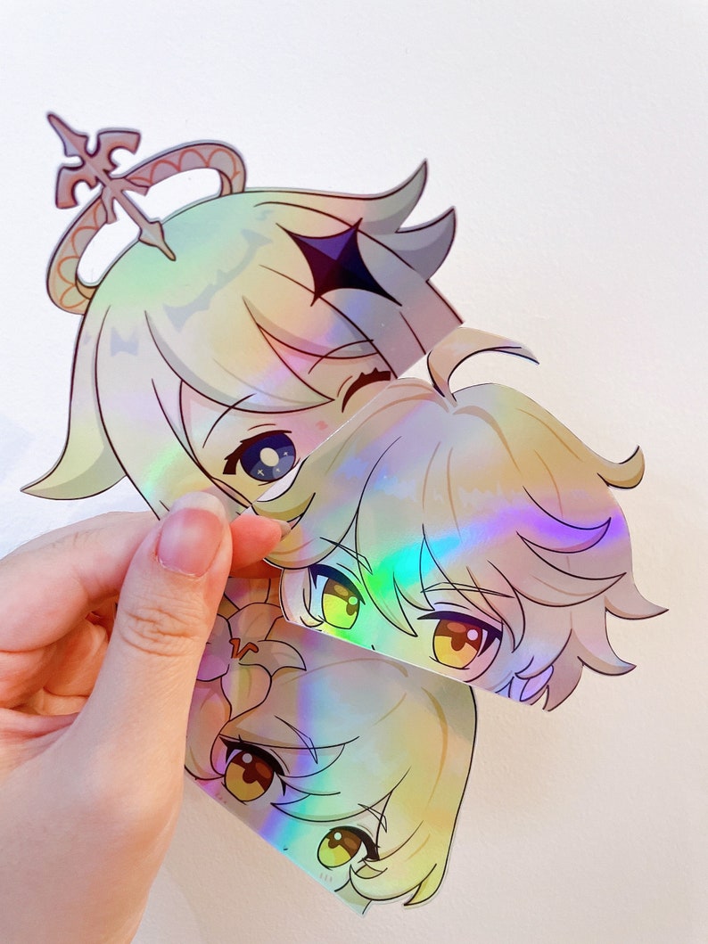 May include: Three iridescent holographic stickers featuring anime-style characters with blonde hair. The characters have large eyes and are smiling. The stickers are cut out and have a glossy finish.