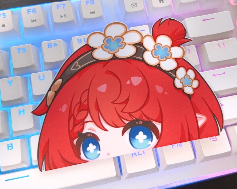 May include: A sticker featuring a cartoon character with bright red hair and large blue eyes. The character has a floral headband with white and blue flowers. The sticker is placed on a white keyboard with blue and purple backlighting.