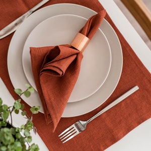 May include: A rust-colored linen placemat with a white plate and a folded linen napkin with a copper napkin ring. A silver fork is placed on the placemat.