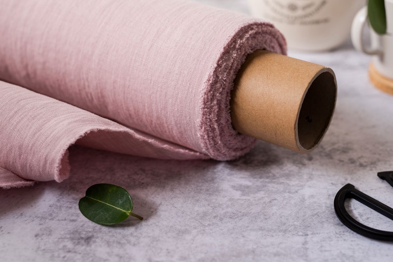 May include: A roll of pale pink fabric is rolled up on a cardboard tube. The fabric is soft and has a slightly textured surface.