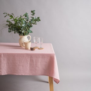 May include: A pink linen tablecloth on a wooden table with a white pitcher, two clear glasses, and a small wooden candle holder. The pitcher has the text "Keep it Real" on it. The table is set for a simple, elegant meal.