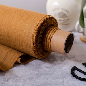 May include: A roll of brown fabric with a frayed edge. The fabric is rolled up on a cardboard tube. The fabric is on a light gray surface.