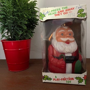 May include: A vintage plastic Santa Claus toy in a clear plastic box. The toy is red and white with a green bag. The box has the text "Press the head and away they go" and "A Play-Friction Toy".