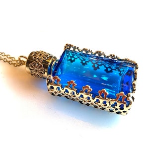 Op de afbeelding: Een gouden ketting met een hanger in de vorm van een blauwe glazen fles. De fles is omhuld door een gouden filigraan frame.