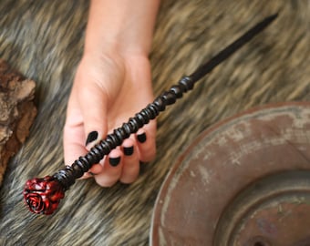 May include: A black and silver hair stick with a red rose detail at the end.