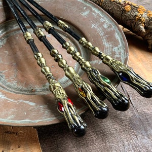 May include: Four black and gold wands with different colored gems at the end. The wands are lying on a copper-colored plate.