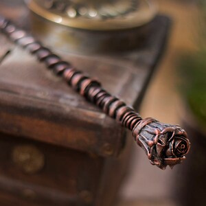 May include: A copper-colored wand with a rose-shaped tip. The wand is made of twisted metal and has a rustic, antique look.