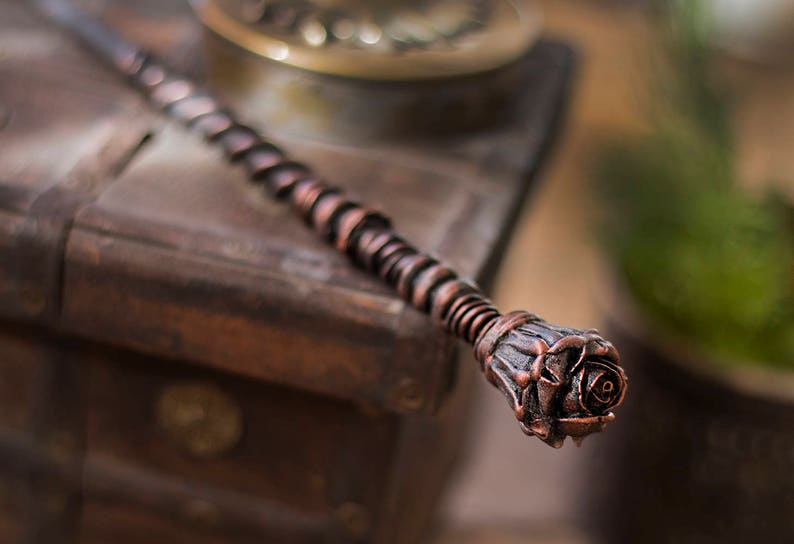 May include: A copper-colored wand with a rose-shaped tip. The wand is made of twisted metal and has a rustic, antique look.
