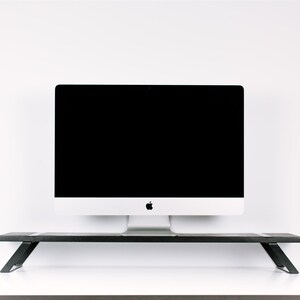 May include: A black metal monitor stand with a white computer monitor on top. The monitor has a black screen and a silver Apple logo.
