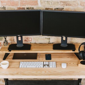 May include: A wooden desk with two black computer monitors, a keyboard, a mouse, a phone, a laptop, a cup of coffee, and a pair of black headphones on a stand.