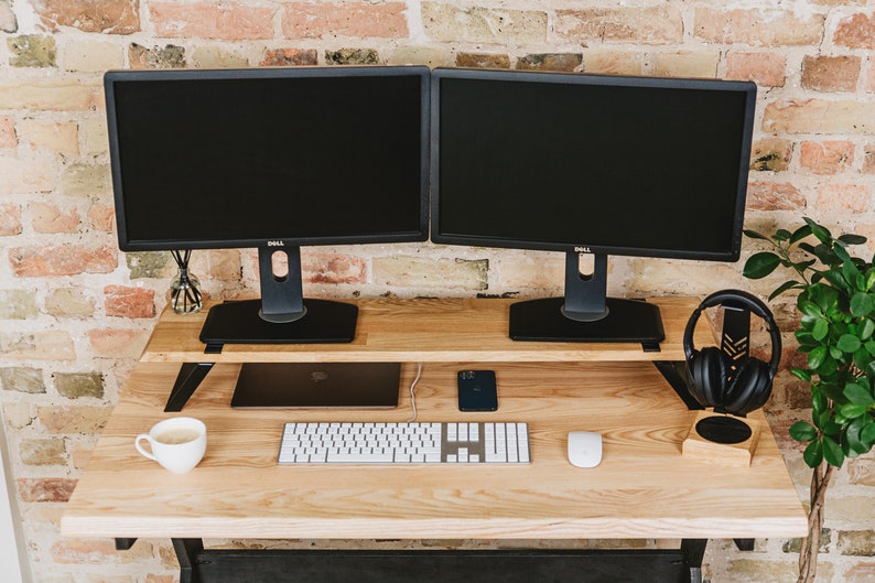 May include: A wooden desk with two black computer monitors, a keyboard, a mouse, a phone, a laptop, a cup of coffee, and a pair of black headphones on a stand.