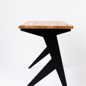 Peut inclure: Un bureau en bois avec un piètement en trépied noir angulaire. Le plateau du bureau est en bois clair avec un motif de grain naturel.