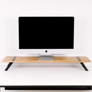 May include: A wooden monitor stand with black metal legs. The stand is made of light wood and has a simple design. A silver computer monitor is sitting on top of the stand.