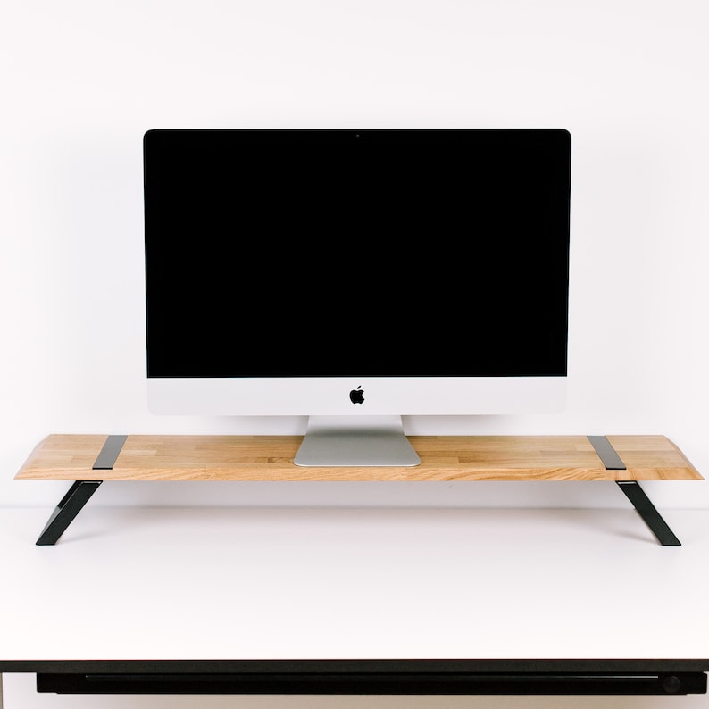 May include: A wooden monitor stand with black metal legs. The stand is made of light wood and has a simple design. A silver computer monitor is sitting on top of the stand.
