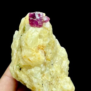 May include: A cluster of clear, white, and yellow crystals with a bright pink ruby crystal on top.