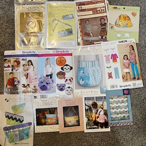 May include: A selection of sewing patterns for bags, purses, and clothing. Brands include Simplicity, Lazy Girl, and Atkinson Designs. The patterns feature a variety of designs and styles. The color scheme includes blues, pinks, and yellows.