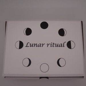 Könnte beinhalten: Eine weiße Karte mit schwarzen Illustrationen verschiedener Mondphasen in einem Kreis. Der Text "Lunar Ritual" ist in Kursivschrift in der Mitte der Karte geschrieben.