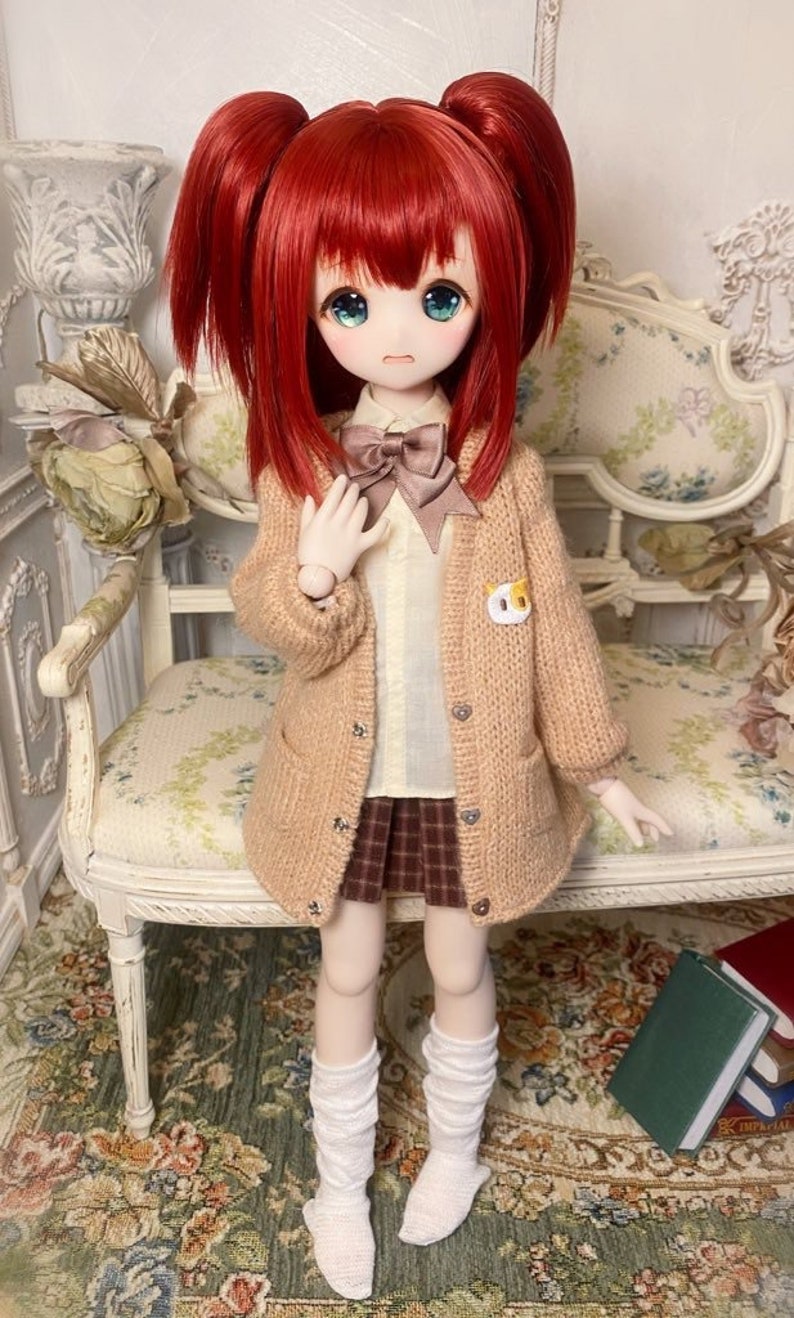 May include: A doll with red hair in pigtails wearing a brown cardigan, a white shirt with a brown bow tie, a plaid skirt, and white knee-high socks.