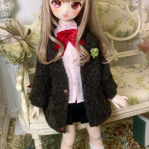 May include: A doll with long blonde hair wearing a brown cardigan, a pink shirt, a black skirt, and white knee-high socks. The doll is sitting on a white chair with a floral pattern.