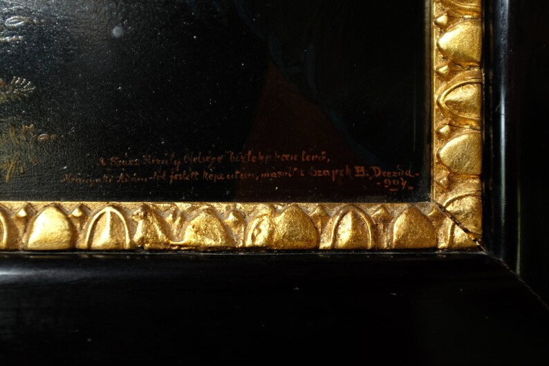 May include: A close-up of a black wooden frame with gold accents. The frame has a gold inscription that reads "Sones Himaly Olelsige bielone been lens, Asantot festett k&eacute;pestre, maroli Gempeh B. Drexia- 105- "