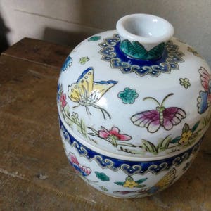 May include: A white porcelain jar with a lid, decorated with colourful butterflies, flowers, and a blue and gold border.