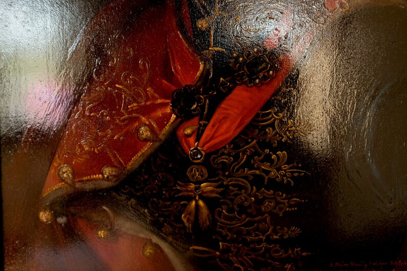 May include: Close-up of a red and gold embroidered fabric with a black and gold patterned background. The fabric has a textured surface and is likely part of a historical costume.