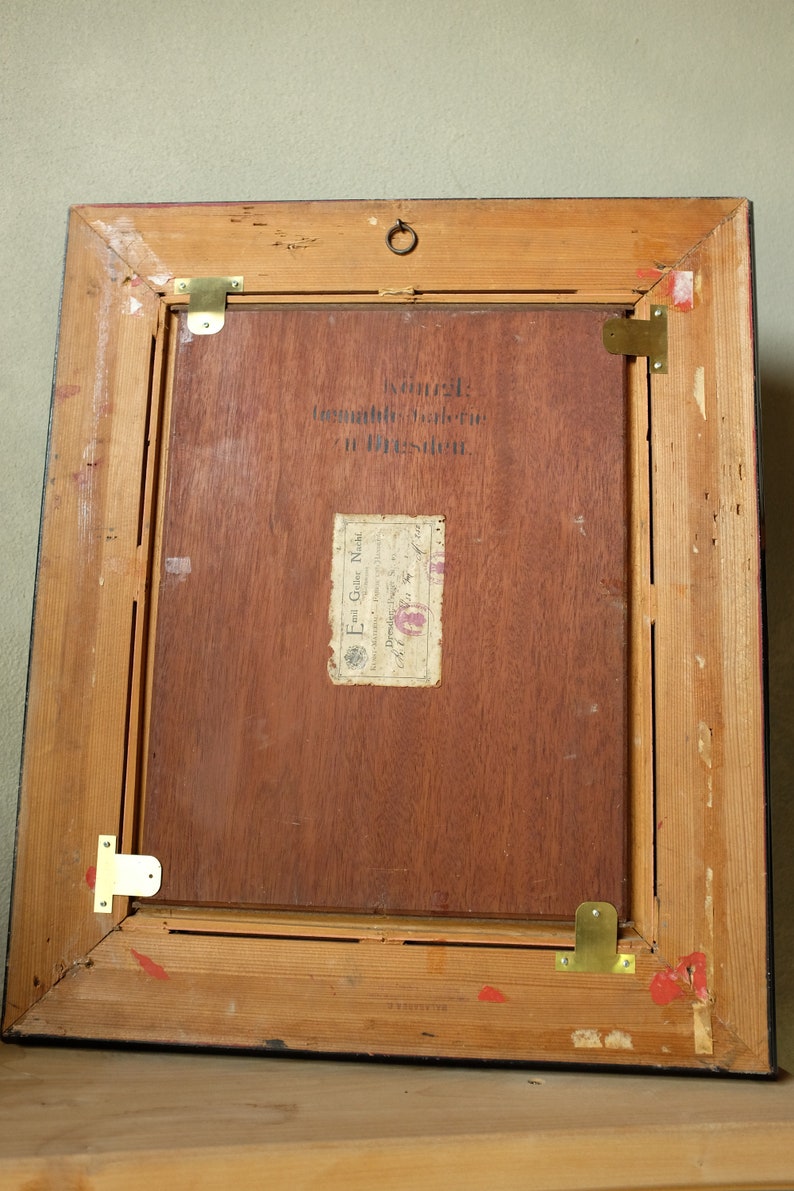 May include: A wooden picture frame with a black border. The back of the frame has a label that reads "Kunstgewerbe-Galerie in Dresden." and "Emil Glog Nachf. Dresden, Germany."