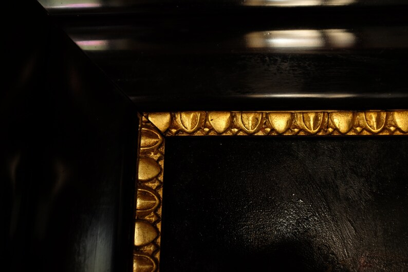 May include: Close-up of a black picture frame with a gold ornate border. The frame is made of wood and has a smooth, polished finish.