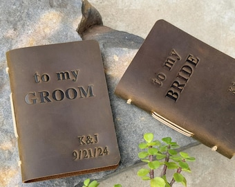 May include: Two brown leather journals with the embossed text "to my GROOM" and "to my BRIDE". The groom's journal includes the initials "K&J" and the date "9/21/24". The journals are bound with cream-colored thread.
