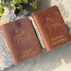 May include: Two brown leather vow books with the words "her vows" and "his vows" engraved on the front. The books are personalised with the names "Jeanna" and "Matthew" and the date "10/26/2024".