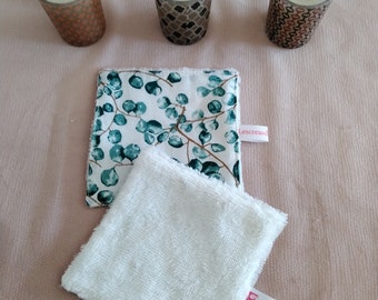 May include: Three small glass candle holders with a white candle in each. The candle holders have a geometric pattern in brown and orange. The candle holders are sitting on a light brown surface. There are two white cotton washcloths with a green and white floral pattern and a white label with the text "Lescreaso" and a white label with the text "Jolos" on the surface.