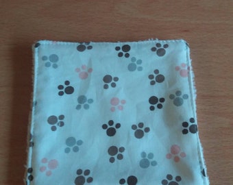 May include: A white washcloth with a light blue background and a pattern of paw prints in grey, black, and pink.