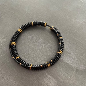 Op de afbeelding: Een zwarte en gouden kralen armband met een dubbelgevouwen ontwerp.