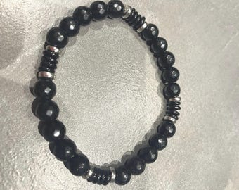 Op de afbeelding: Zwart kralenarmband met facetkralen en zilverkleurige metalen accenten. De armband heeft een stretch design, met een mix van ronde en cilindrische kralen. Een eenvoudig, elegant sieraad.