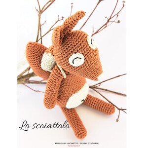 Op de afbeelding: Een gehaakt amigurumi-speelgoed eekhoorn met bruine vacht, witte accenten en zwarte ogen. Het speelgoed zit op een tak.