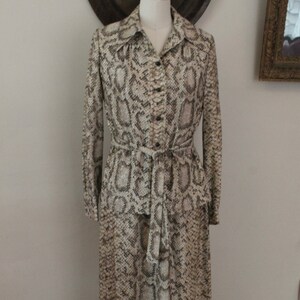 May include: A long-sleeved dress with a snakeskin print in shades of brown and white. The dress has a collared neckline, button closure, and a matching belt.