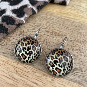 Puede incluir: Un par de pendientes de plata con un diseño redondo de estampado de leopardo negro, naranja y blanco.