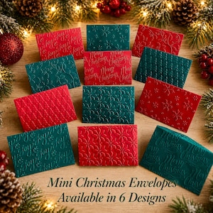 May include: A collection of rectangular mini envelopes in red and dark green, featuring embossed patterns including snowflakes, poinsettias, diamond grids, and script text reading Merry Christmas and joy. The envelopes are arranged in a group.