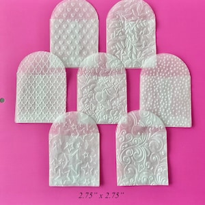 May include: Eight white, translucent, 2.75 inch by 2.75 inch,  envelopes with different embossed patterns. The patterns include hearts, flowers, stars, and swirls.