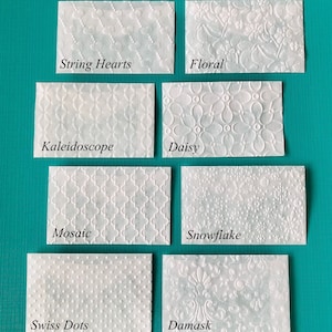 May include: A set of ten white embossed paper cards with different patterns. The patterns include string hearts, floral, kaleidoscope, daisy, mosaic, snowflake, swiss dots, and damask.