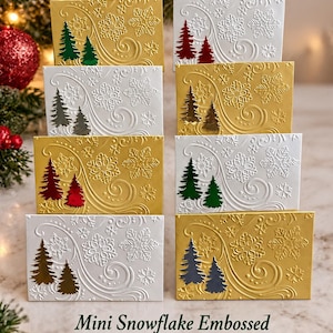 May include: A collection of mini gift card envelopes featuring embossed snowflake and swirl patterns. Each envelope displays two small, colored pine trees. The envelopes are available in gold and white, with various tree colors including green, red, and blue.