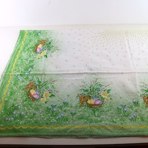 Könnte beinhalten: Weiße Tischdecke mit grünem Rand und einem sich wiederholenden Muster von Hasen, die Körbe mit Ostereiern halten. Die Tischdecke hat einen weißen Hintergrund mit einem dezenten gelben Punktmuster.