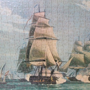 K&ouml;nnte beinhalten: Ein Vintage-Puzzle, das eine Seeschlacht mit mehreren Segelschiffen im Wasser darstellt. Die Schiffe haben wei&szlig;e Segel und feuern Kanonen aufeinander ab. Der Himmel ist hellblau mit wei&szlig;en Wolken.