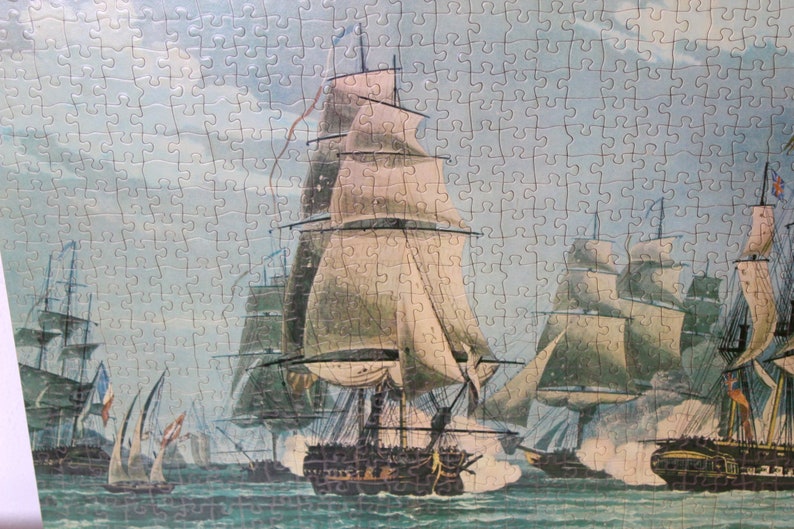 K&ouml;nnte beinhalten: Ein Vintage-Puzzle, das eine Seeschlacht mit mehreren Segelschiffen im Wasser darstellt. Die Schiffe haben wei&szlig;e Segel und feuern Kanonen aufeinander ab. Der Himmel ist hellblau mit wei&szlig;en Wolken.