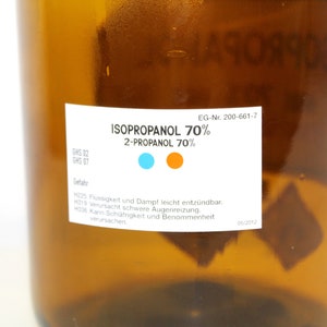 Puede incluir: Una botella de vidrio marr&oacute;n con una etiqueta blanca que dice "ISOPROPANOL 70% 2-PROPANOL 70%". La etiqueta tambi&eacute;n incluye el texto "GHS 02 GHS 07 EG-Nr. 200-661-7" e informaci&oacute;n de seguridad en alem&aacute;n.