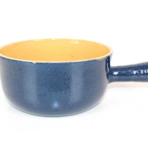Könnte beinhalten: Ein blauer Keramik-Fonduetopf mit gelbem Innenraum und einem Griff.