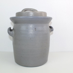 Op de afbeelding: Een grijze keramische pot met een deksel en twee handvatten. De pot heeft het nummer "6" aan de zijkant.