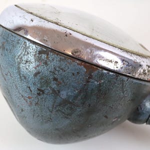 Puede incluir: Un faro de coche vintage, redondo, azul y cromado, con una base de metal y un borde cromado. El faro tiene un aspecto desgastado y envejecido, con arañazos y marcas en la superficie.