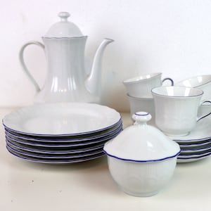 Puede incluir: Un juego de té de porcelana blanca con ribete azul. El juego incluye una tetera, un azucarero, una jarra de crema, seis tazas y seis platillos.