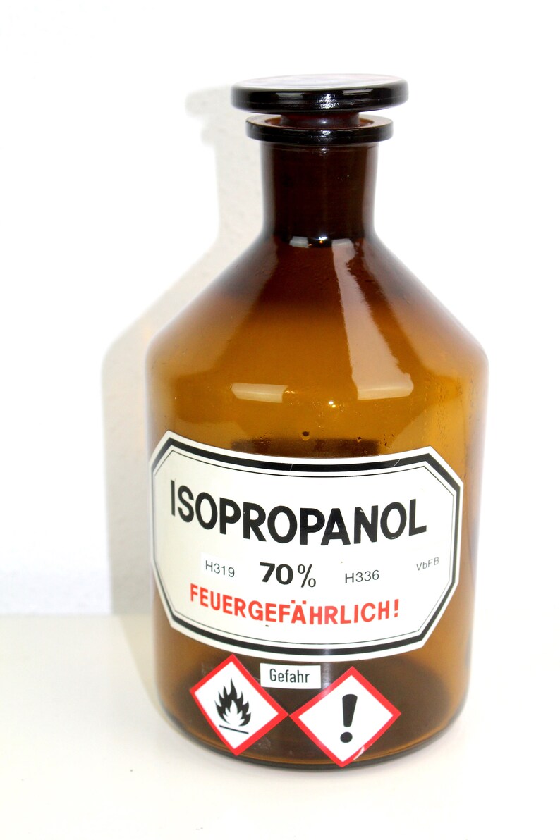 Puede incluir: Una botella de vidrio marr&oacute;n con una tapa negra, etiquetada "ISOPROPANOL 70% H319 H336 VbF B FEUERGEF&Auml;HRLICH!" con un s&iacute;mbolo de llama roja y blanca y un signo de exclamaci&oacute;n.